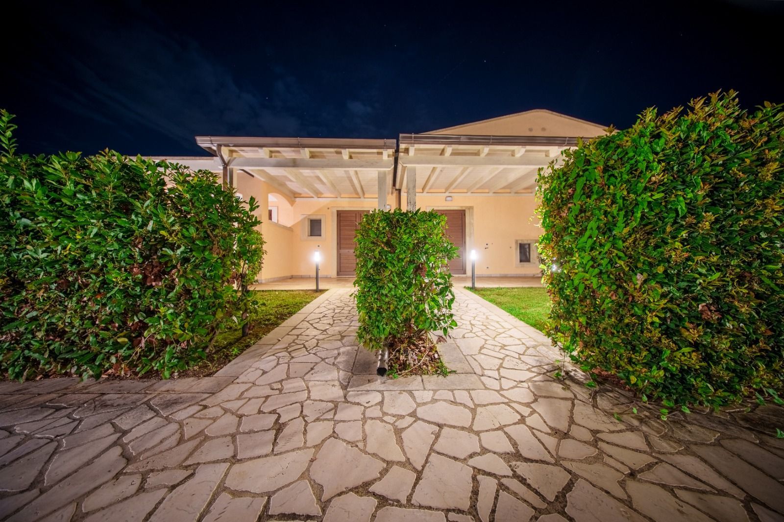 Vista notturna di una casa con sentiero in pietra e cespugli potati che conducono all'ingresso.