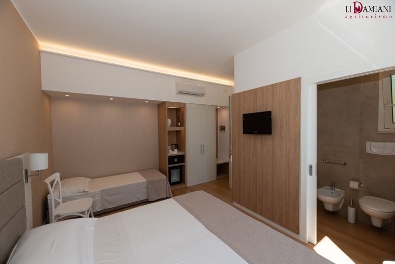 Camera d'albergo con letto matrimoniale, letto singolo e bagno. Toni neutri e luce naturale.