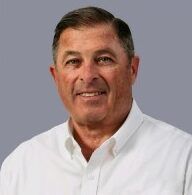 Man with short brown hair, smiling, wearing a white button-down shirt.