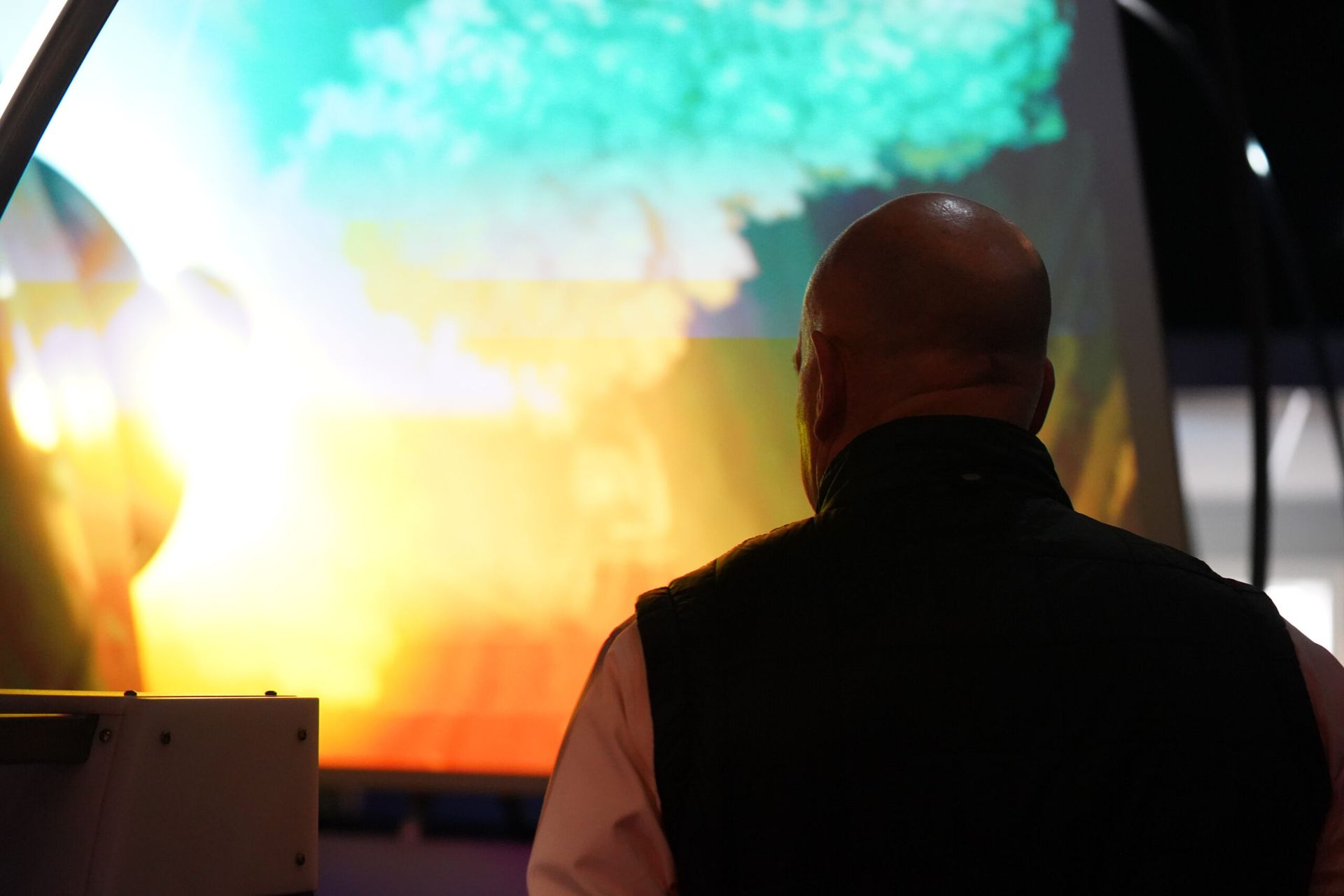 Man in vest looking at a colorful projection of light and shapes on a large screen.