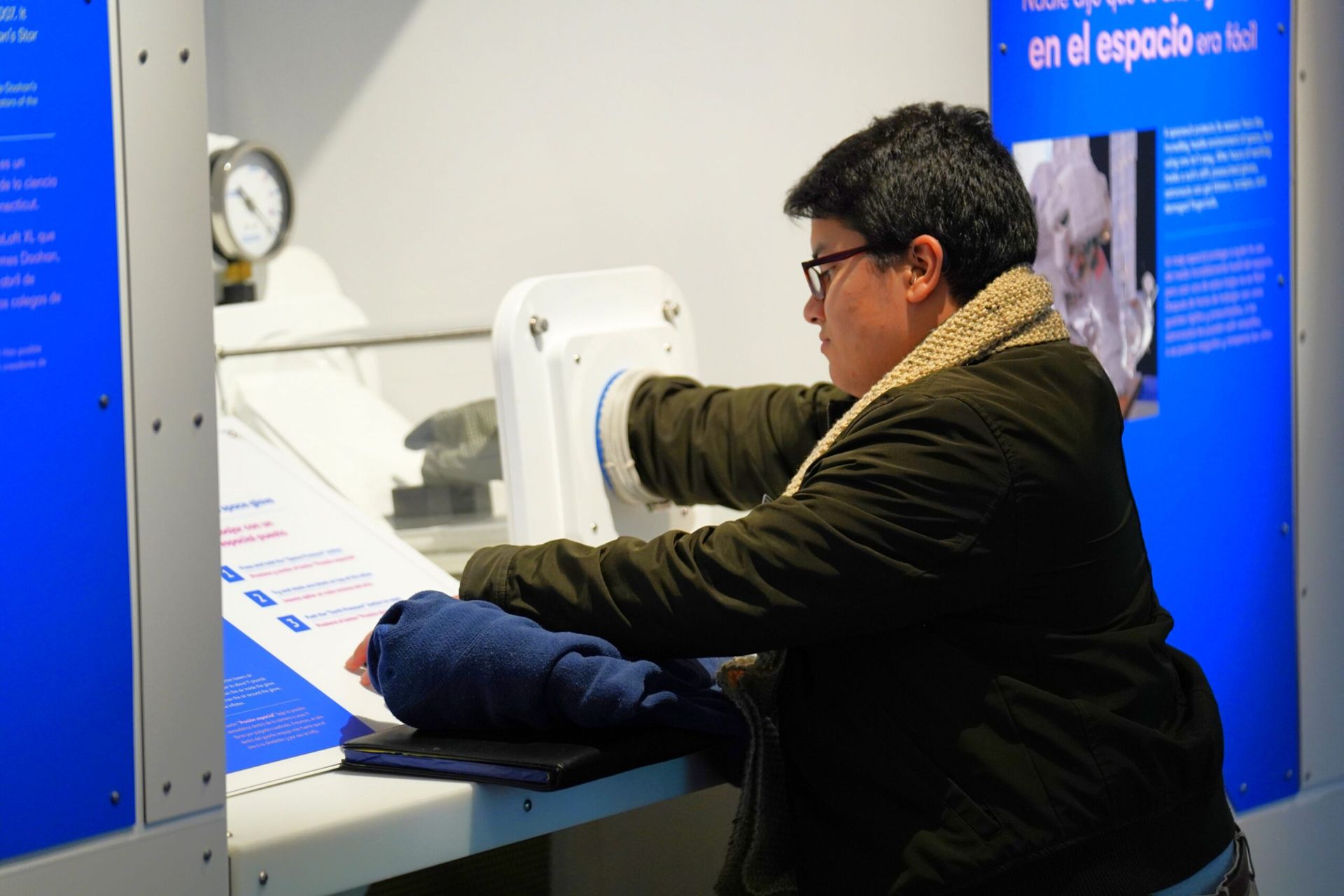 Person using exhibit with attached gloves. Exhibit has pressure gauge and blue informational panels.