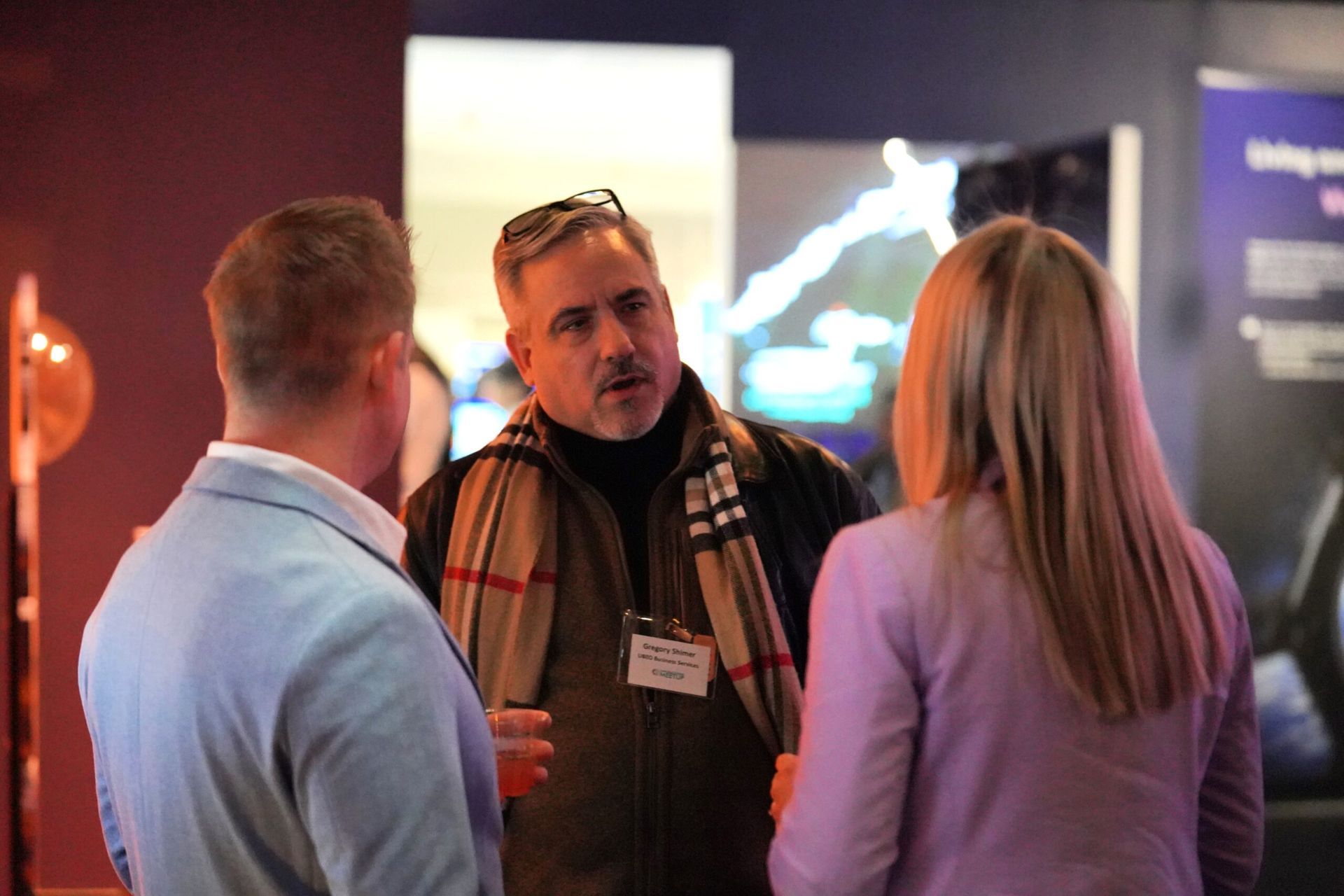 Three people in a room are in conversation. Man in center gestures while speaking.