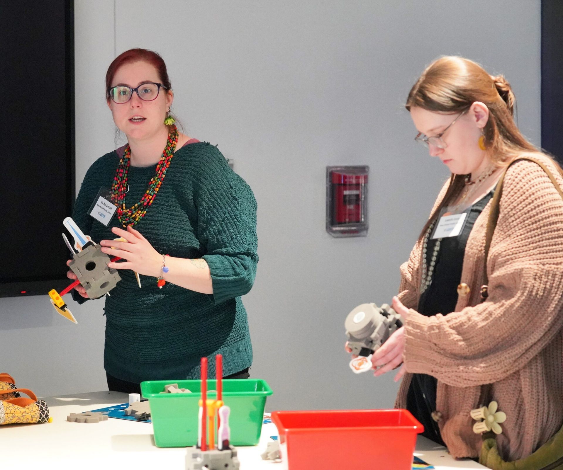 Two people working with LEGOs at a table; one holds a completed model, the other assembles pieces.