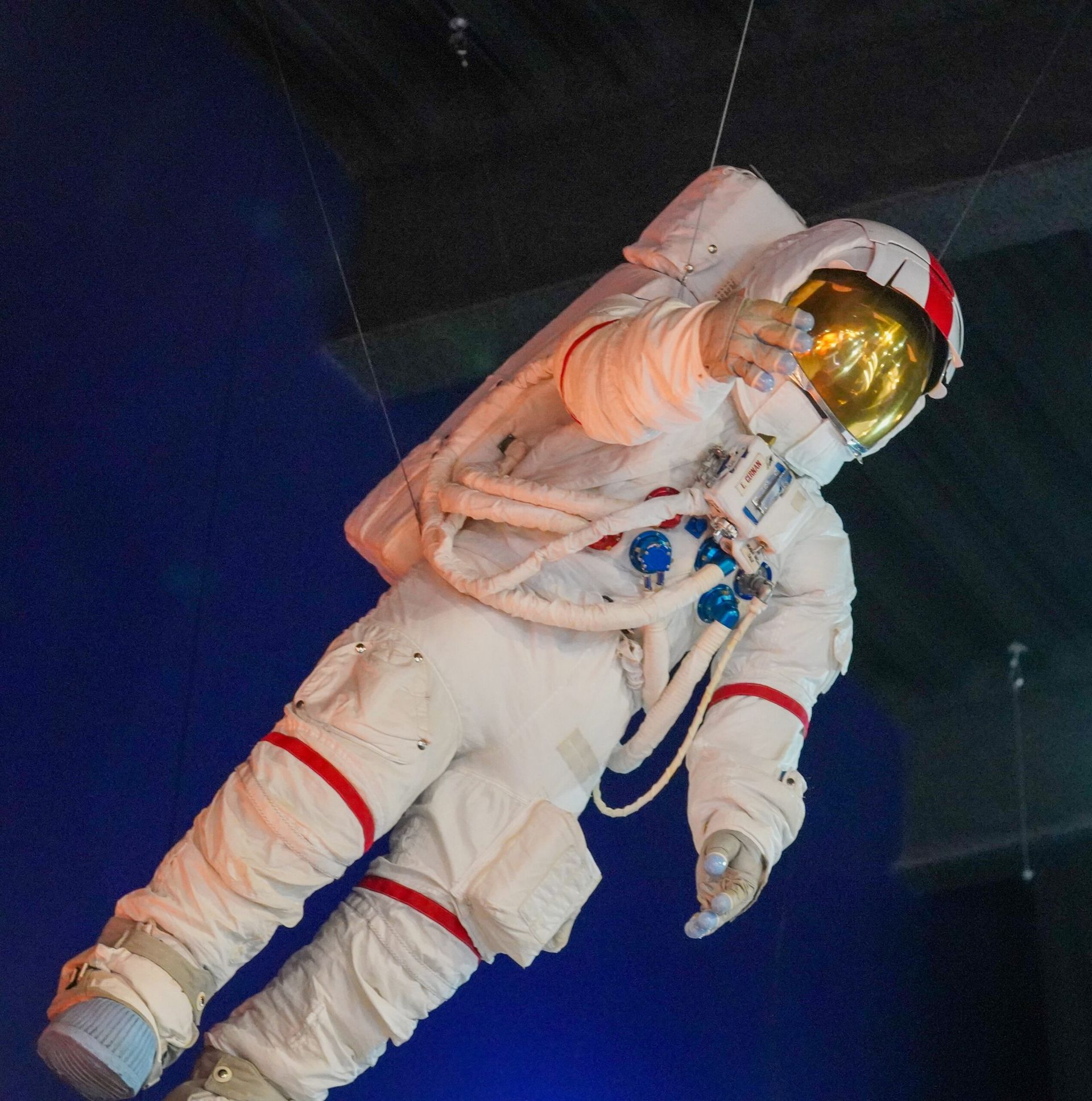 Astronaut in white spacesuit, gold visor, floating against a dark blue background, gesturing.