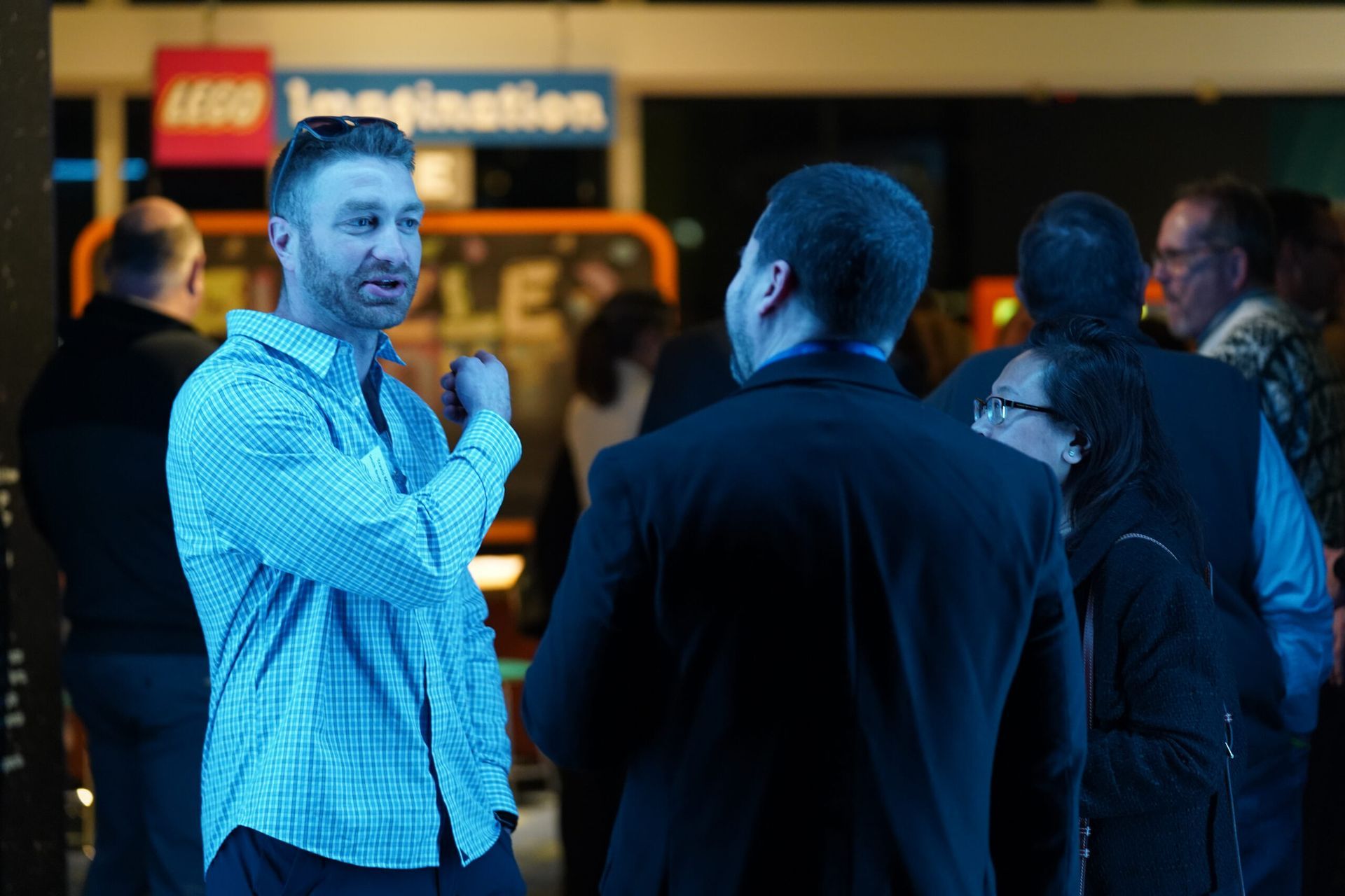 Two men talking, one in blue checkered shirt, others in dark attire, near 