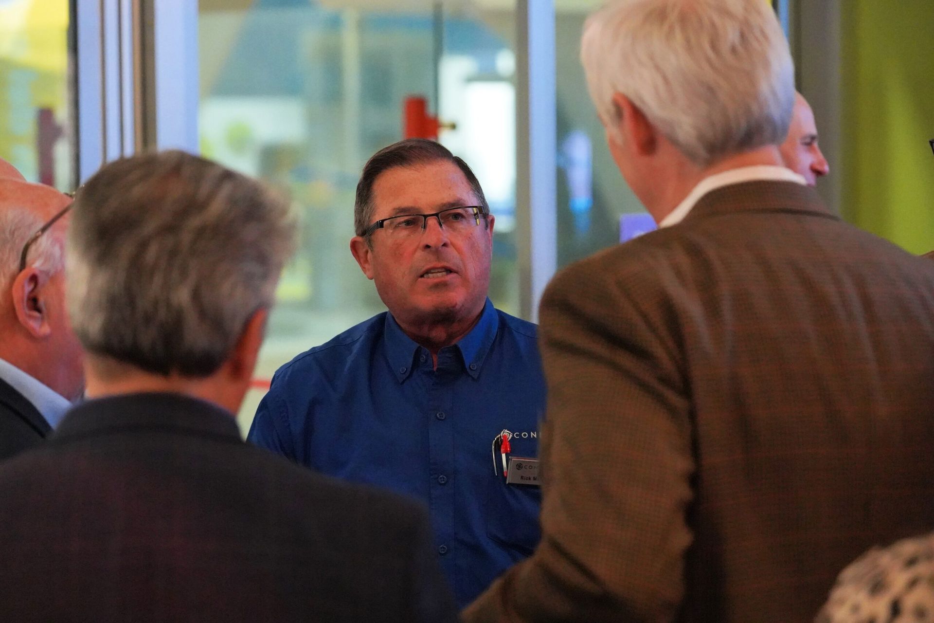 Man in blue shirt speaks with others in a brightly lit room.
