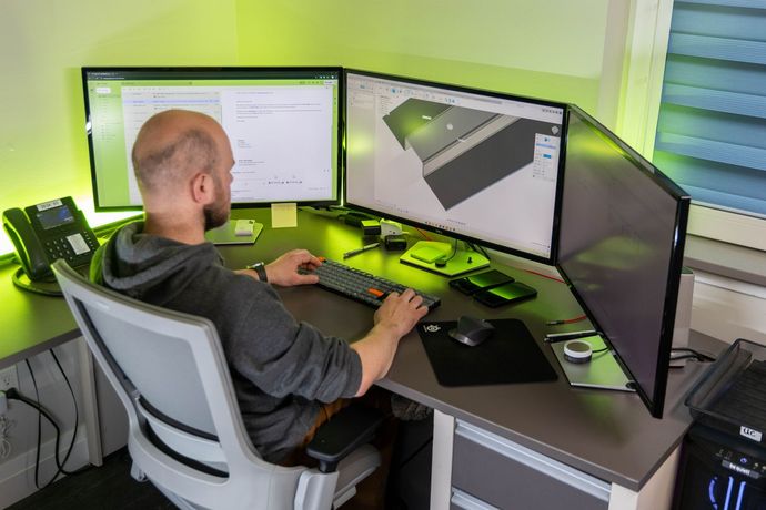 Man working at a desk with three monitors, a keyboard, and a mouse; lit with green light symbolizing Accelerating Strategic Growth.