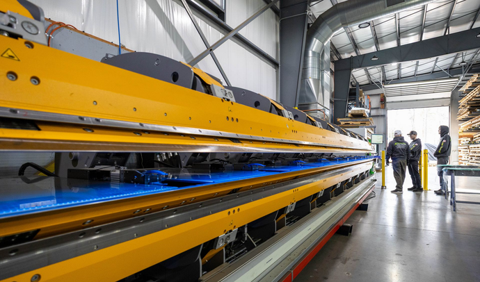 Yellow industrial machine in a factory with three people observing symbolizing  Driving Operational Excellence.