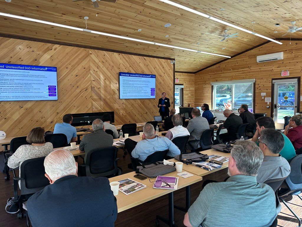 People attending a presentation in a wood-paneled room, with two screens displaying information.