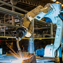 Welding robot in an industrial setting; sparks fly from a weld point.