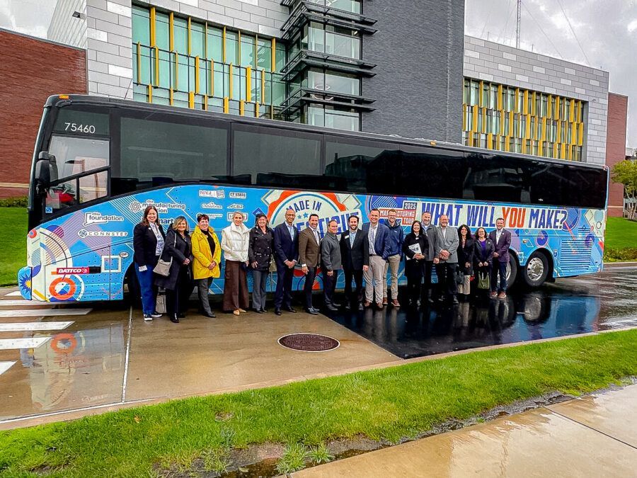 Group poses beside a colorful bus in front of a modern building.