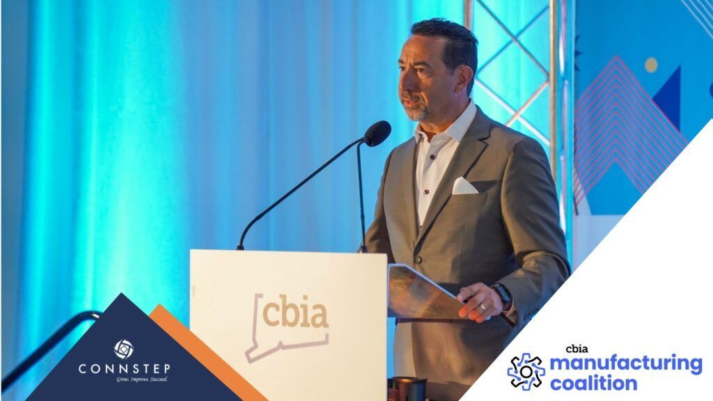 Man speaking at a podium with a microphone. The event backdrop features text and logos.