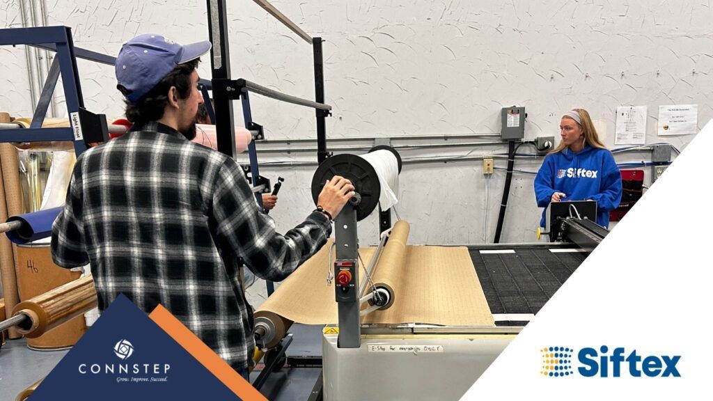 Man operating a machine with a roll of paper, another person nearby. Industrial setting, Siftex logo.