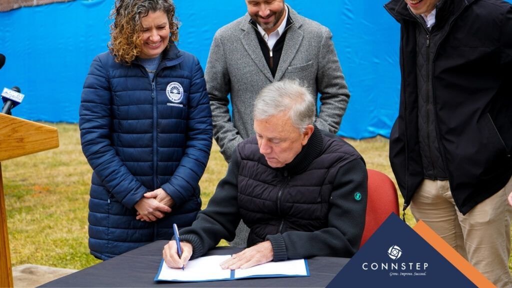 Man signing document at a table, surrounded by three people outdoors.