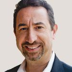 Smiling man with short dark hair, goatee, wearing a dark blazer over a white shirt.