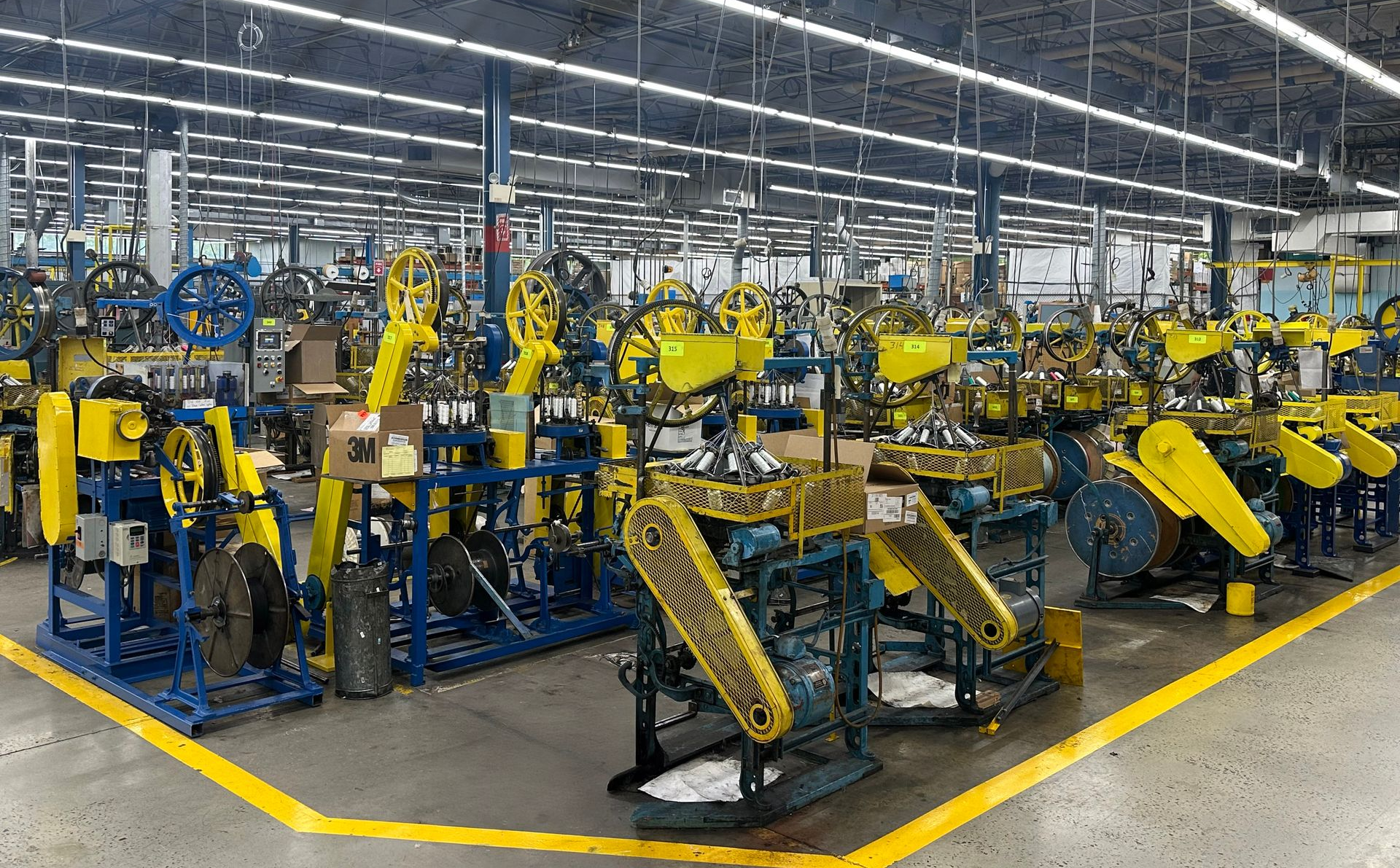 Factory floor with rows of industrial machines, blue and yellow, under bright lights.
