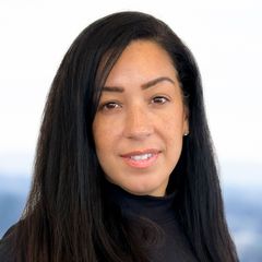 A portrait of Carissa Roman, Continuous Improvement at CONNSTEP, smiling, wearing a black turtleneck, looking at the viewer. Blurred background.