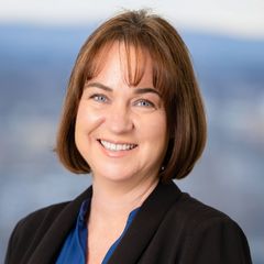 A portrait of Caroline Bernardoni, Director, Human Resources at CONNSTEP, smiling, wearing a blue shirt and black blazer, with a blurred cityscape background.