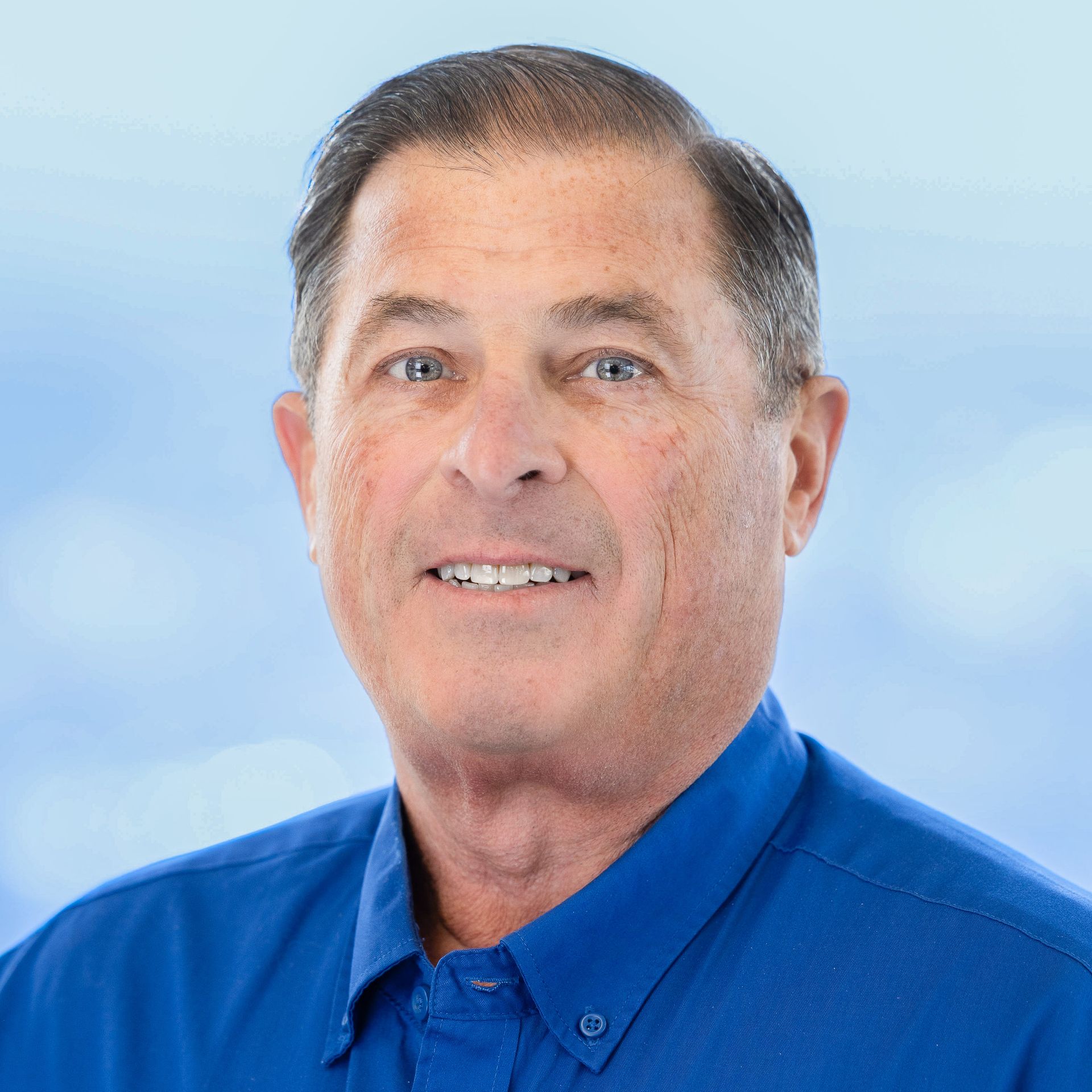 Man in a blue shirt smiles at the camera against a blue and white background.
