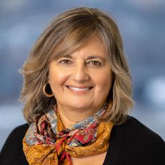 A portrait of Bernice Zampano, Strategic Relationship Manager at CONNSTEP, with shoulder-length blonde hair smiling, wearing a colorful scarf and black top, set against a blurred background.