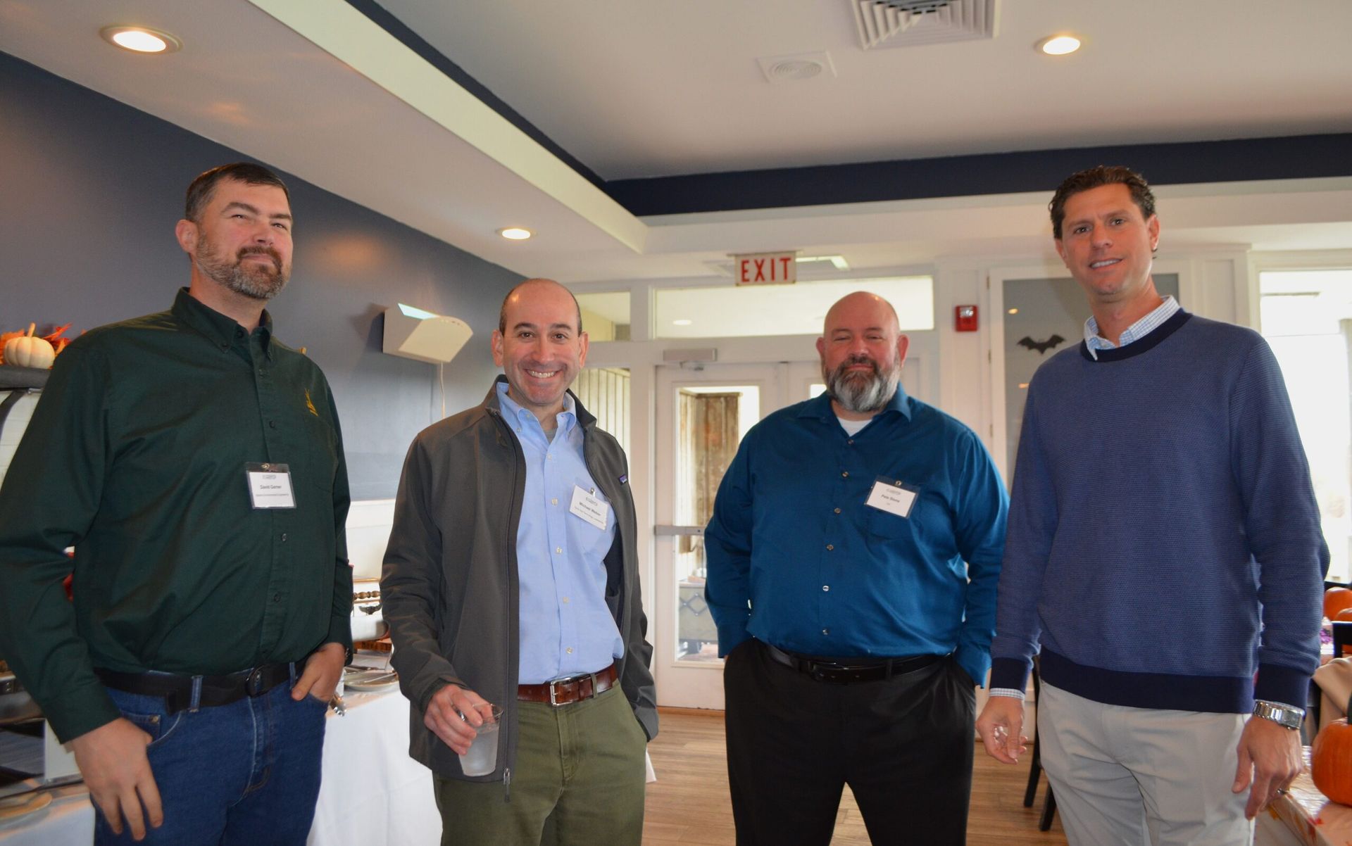 Four men in a room, two with beards, wearing casual attire, some with name tags.