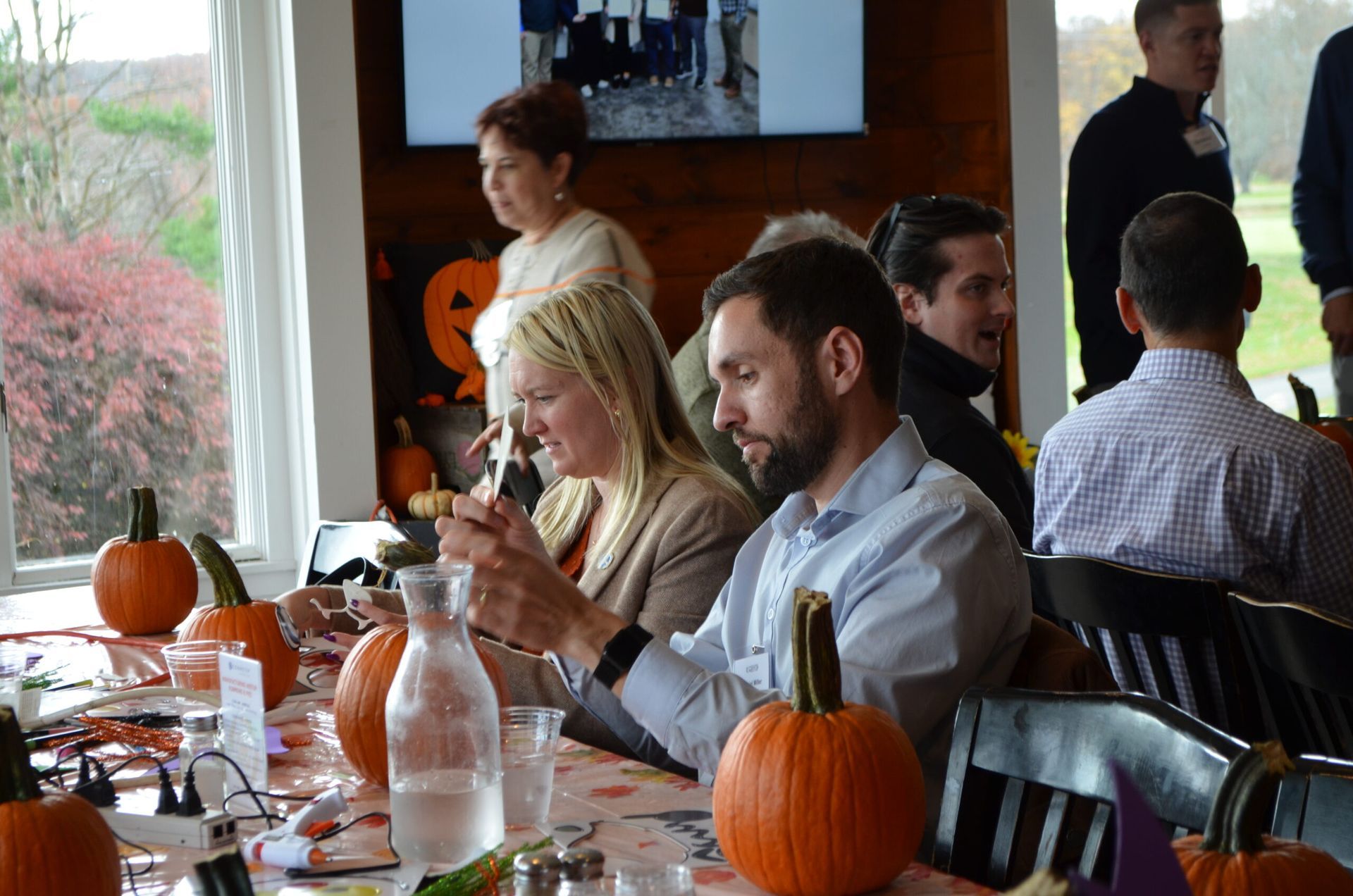 People at a table with pumpkins, eating and looking at phones, likely a fall gathering.