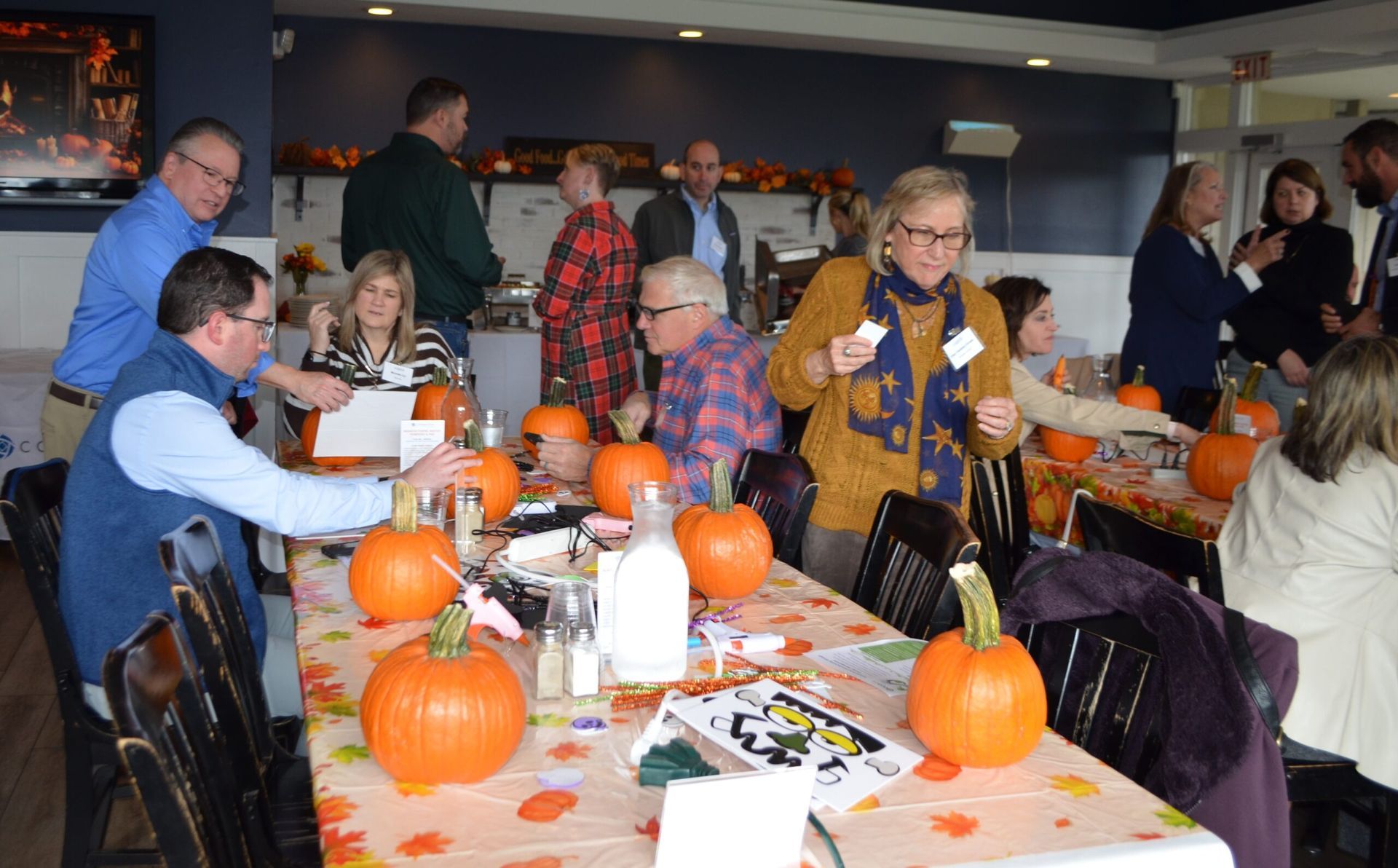 People carving pumpkins at a decorated table; gathering in a room.