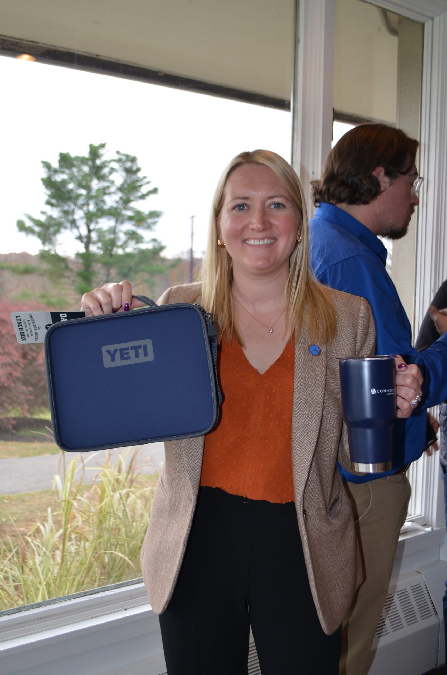 Woman holding a blue Yeti lunch bag and tumbler, smiling, in front of a window.