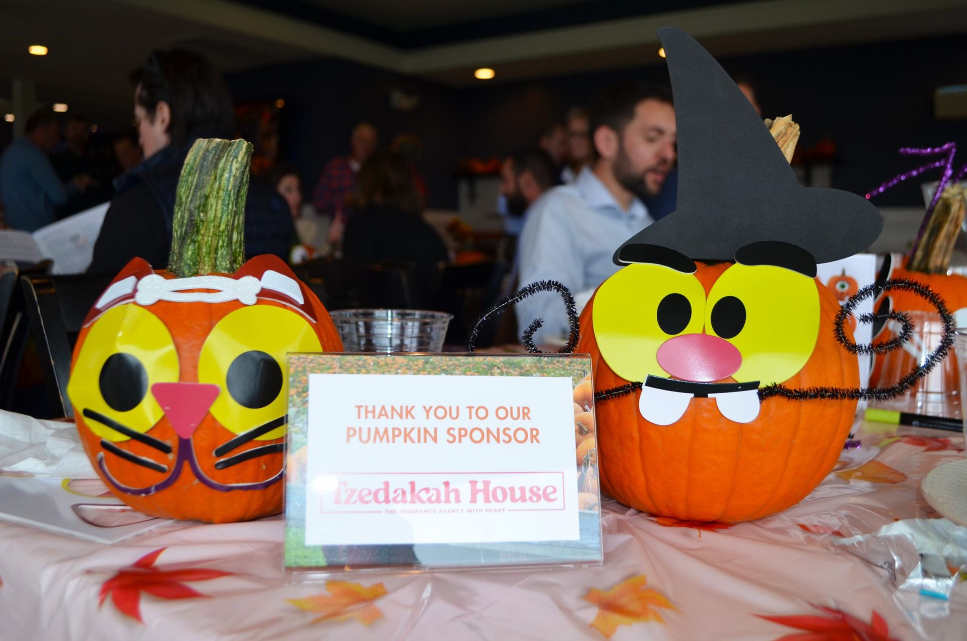 Two decorated pumpkins with a sign thanking a sponsor at an event.