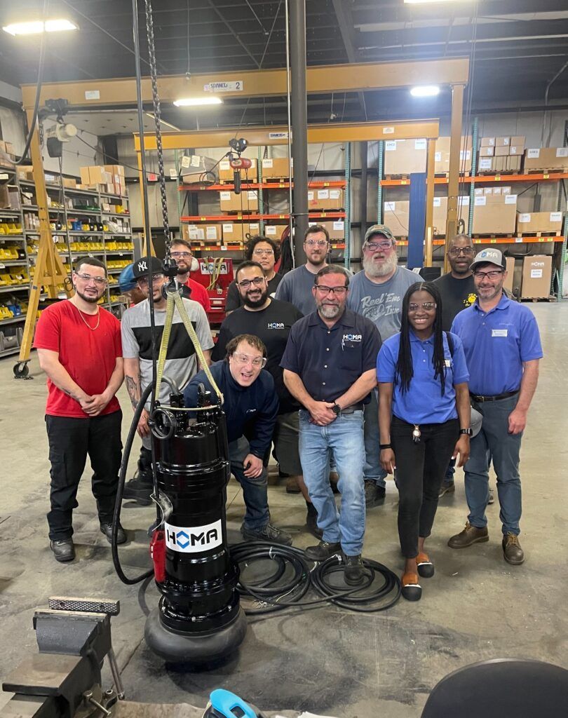 Group of people standing with a large black pump in a warehouse setting.