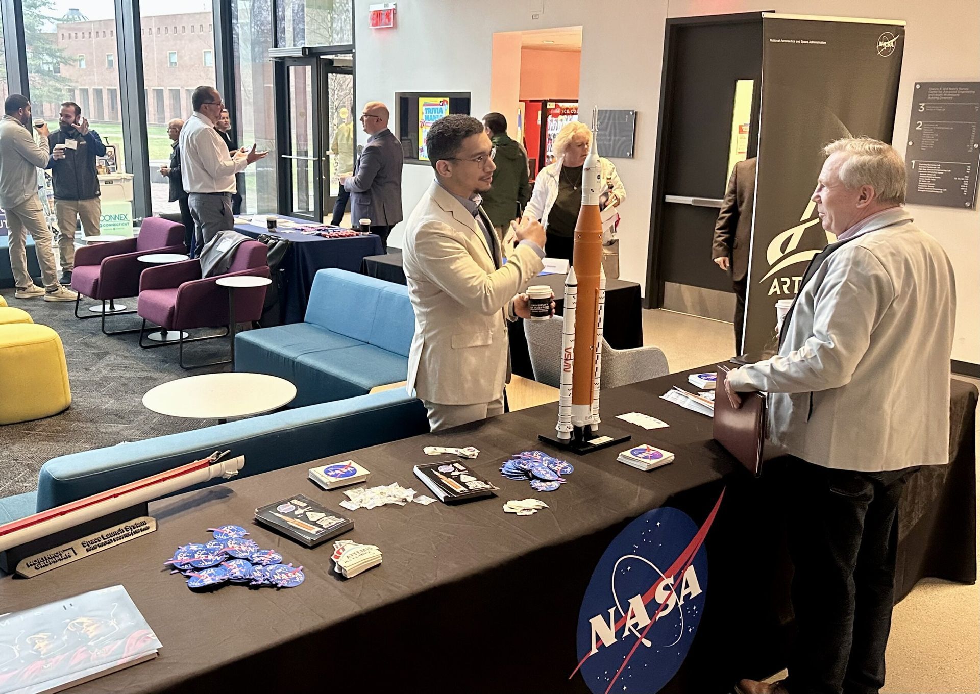 People at a NASA event, near a table with models and brochures, inside a modern building.