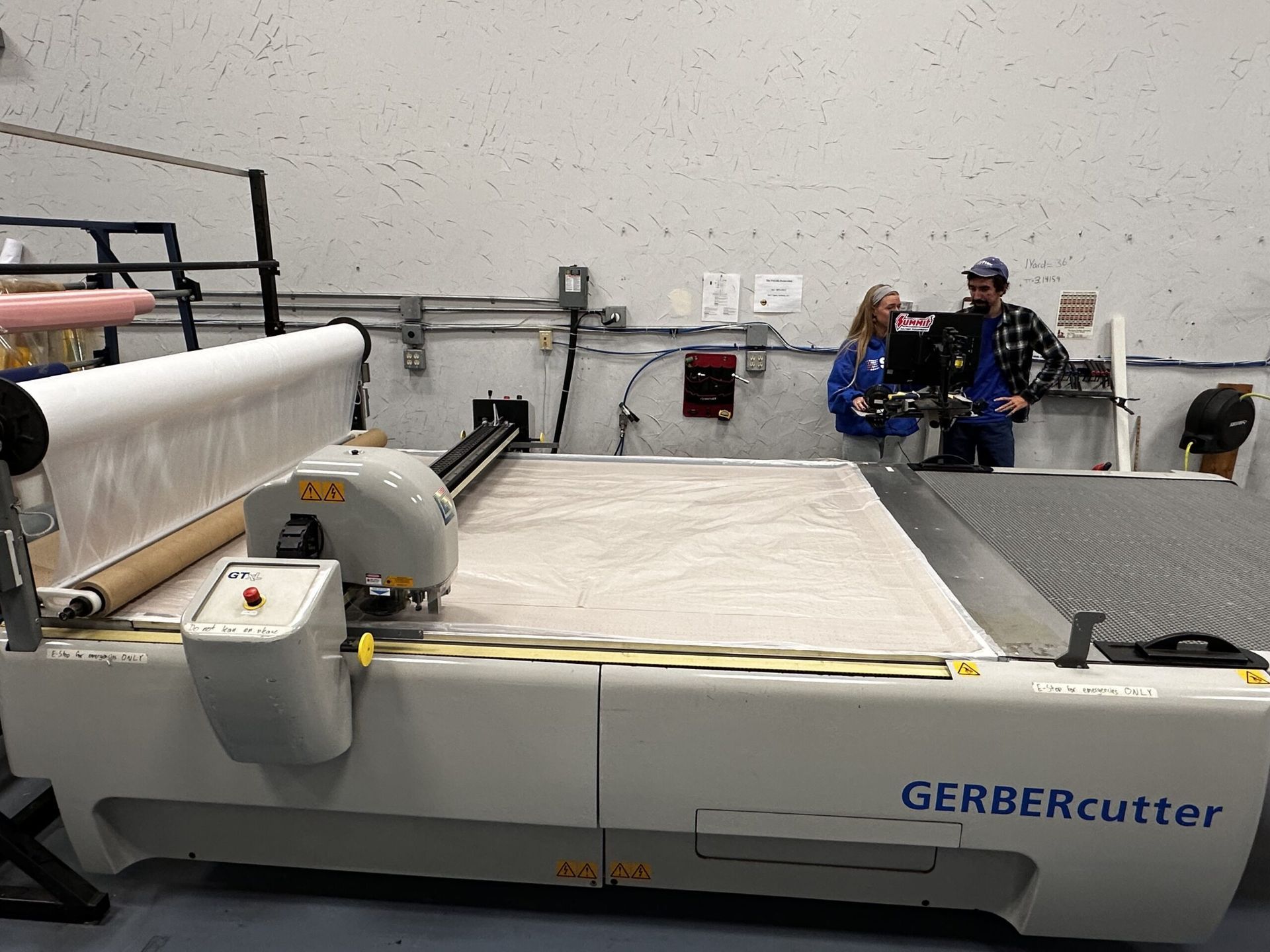 A large GERBERcutter machine in a factory setting, with two people looking at the machine.