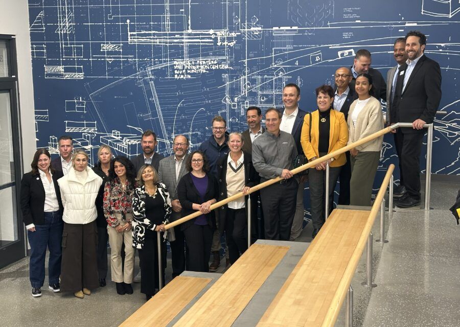 Group of people posing on stairs in front of a blue blueprint wall.