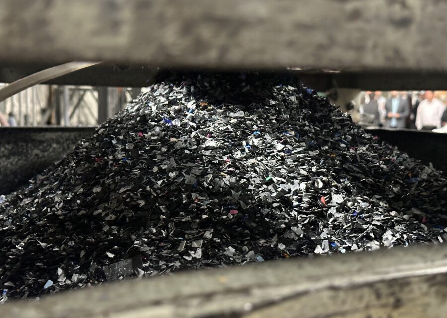 Pile of shredded black plastic inside a metal machine, likely for recycling.