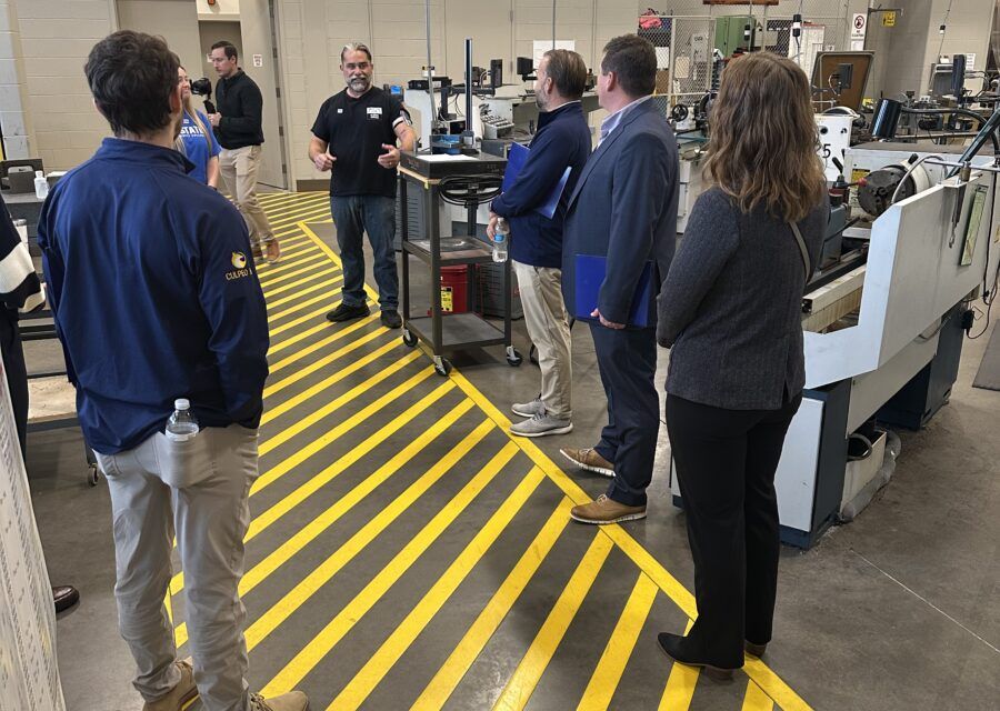 Group of people listening to a person giving a presentation in a workshop with machinery.