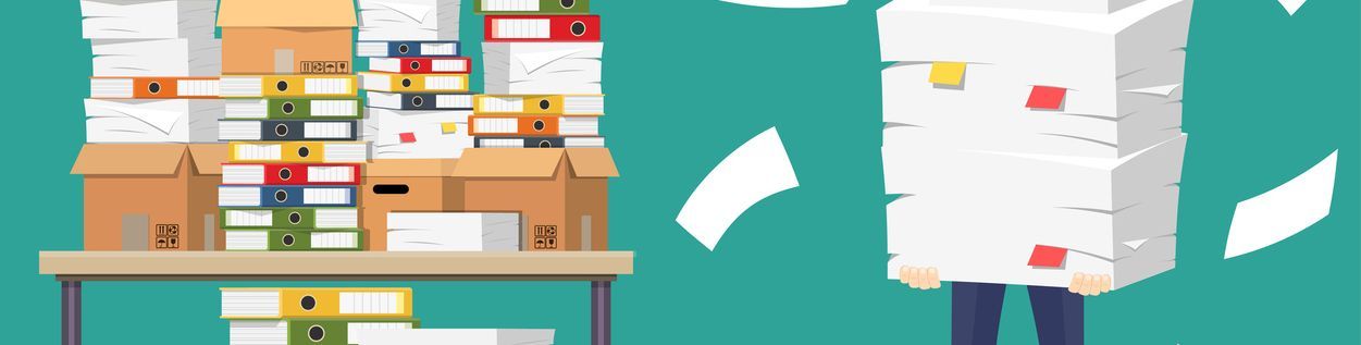 A person is buried in a large stack of papers, next to a table of overflowing boxes of paperwork.