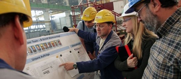 Group of people in hard hats looking at a large printed document in a factory setting.