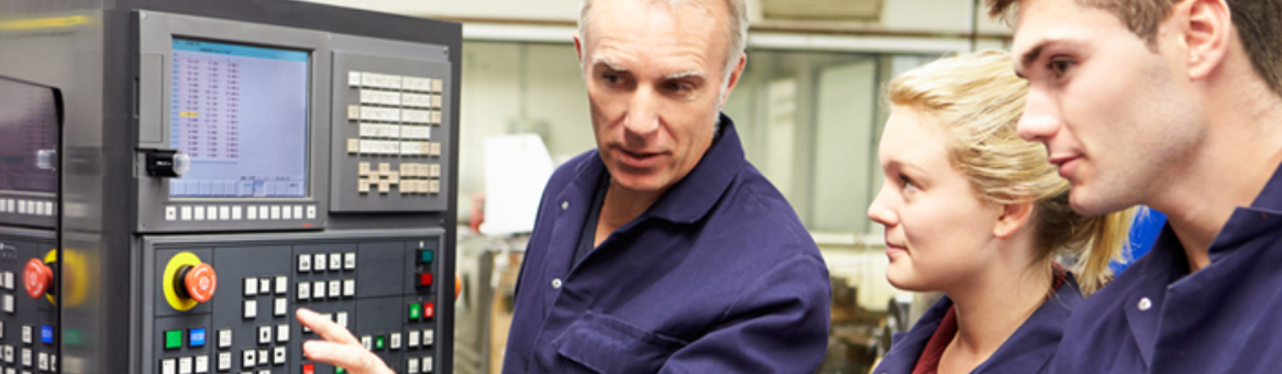 Three people in blue work shirts looking at a machine’s control panel. The central man points, while the other two observe.