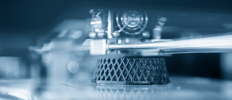 Close-up of a 3D printer head depositing material to create a honeycomb-patterned object.