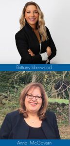 Two women, one with blonde hair, arms crossed, and the other wearing glasses, smiling.