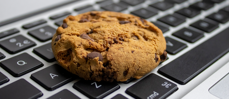 A chocolate chip cookie sits on a laptop keyboard.