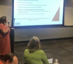 Two women present to an audience in a room with a presentation on a screen.