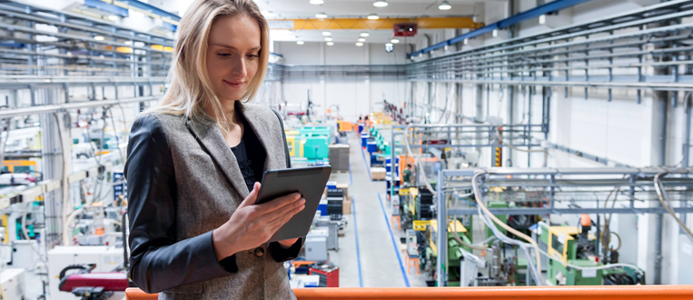 Woman in a factory looking at a tablet, surrounded by machinery.