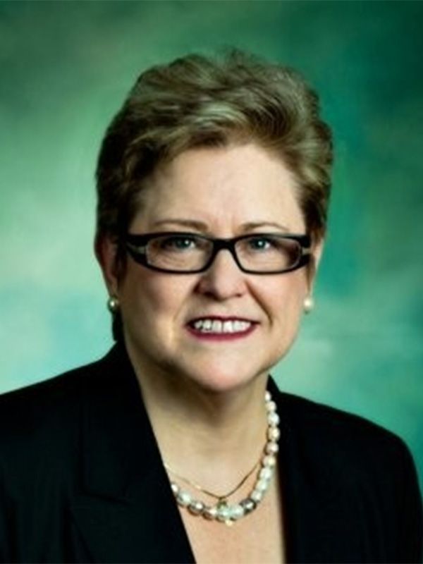 A woman wearing glasses and a pearl necklace smiles for the camera