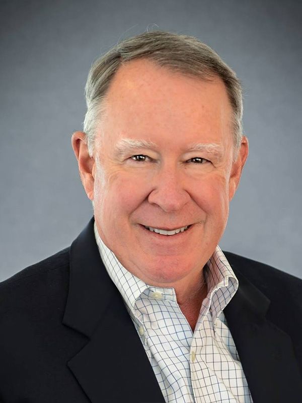 A man in a suit and plaid shirt is smiling for the camera.