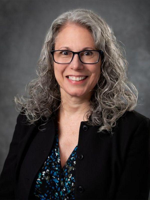 A woman wearing glasses and a black jacket is smiling for the camera.