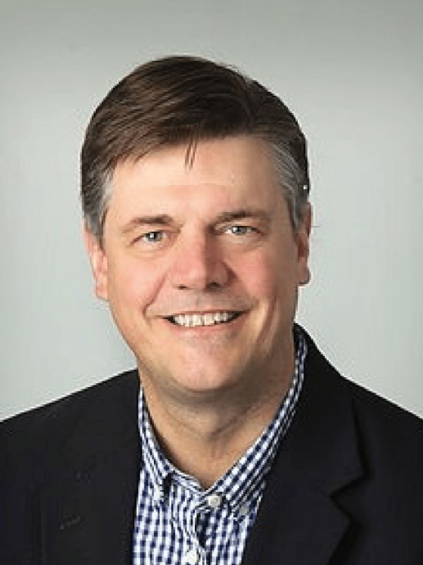 A man in a suit and plaid shirt is smiling for the camera.