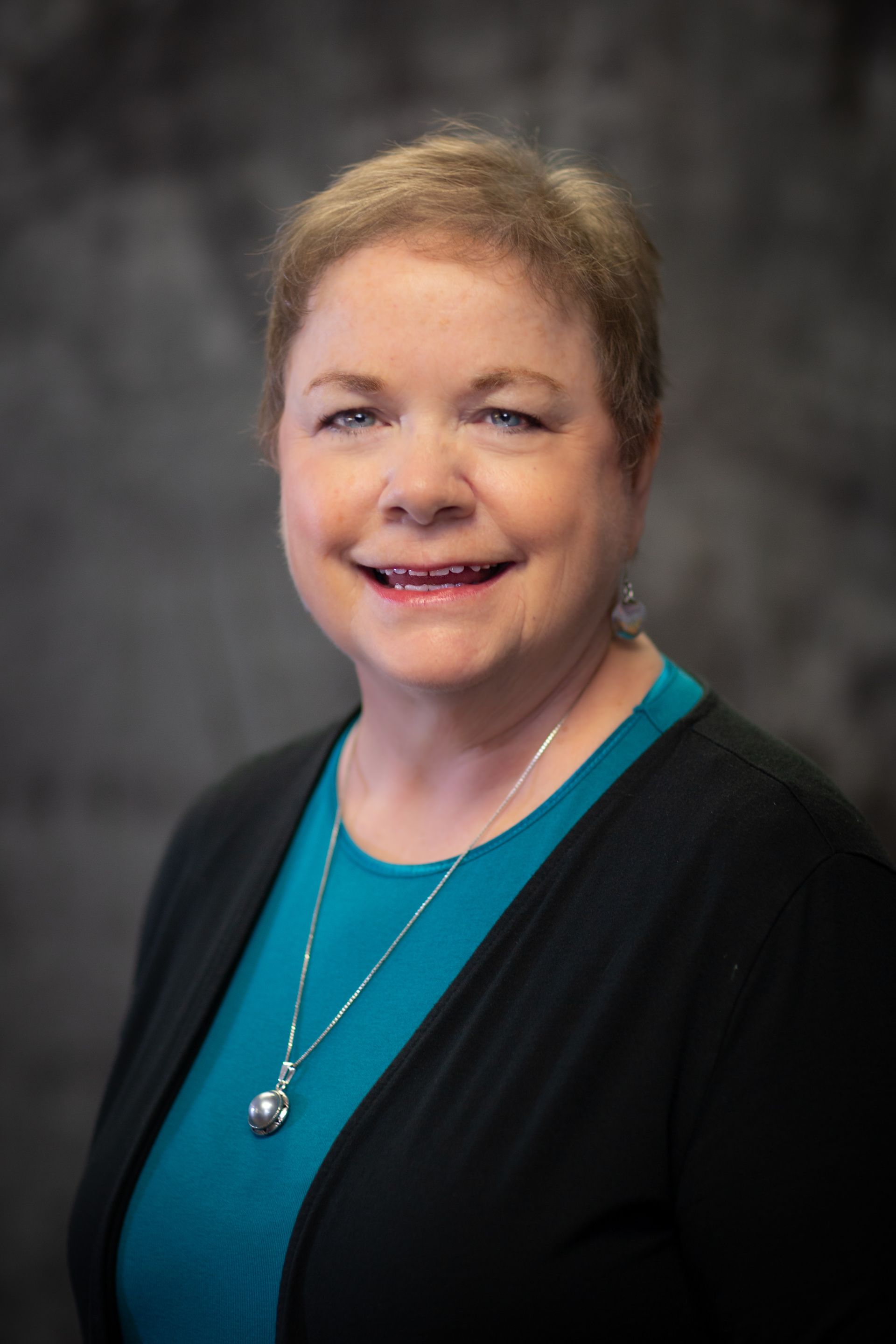 A woman wearing a blue shirt and a black sweater is smiling for the camera.
