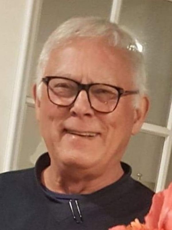 A man wearing glasses is smiling and holding a flower.