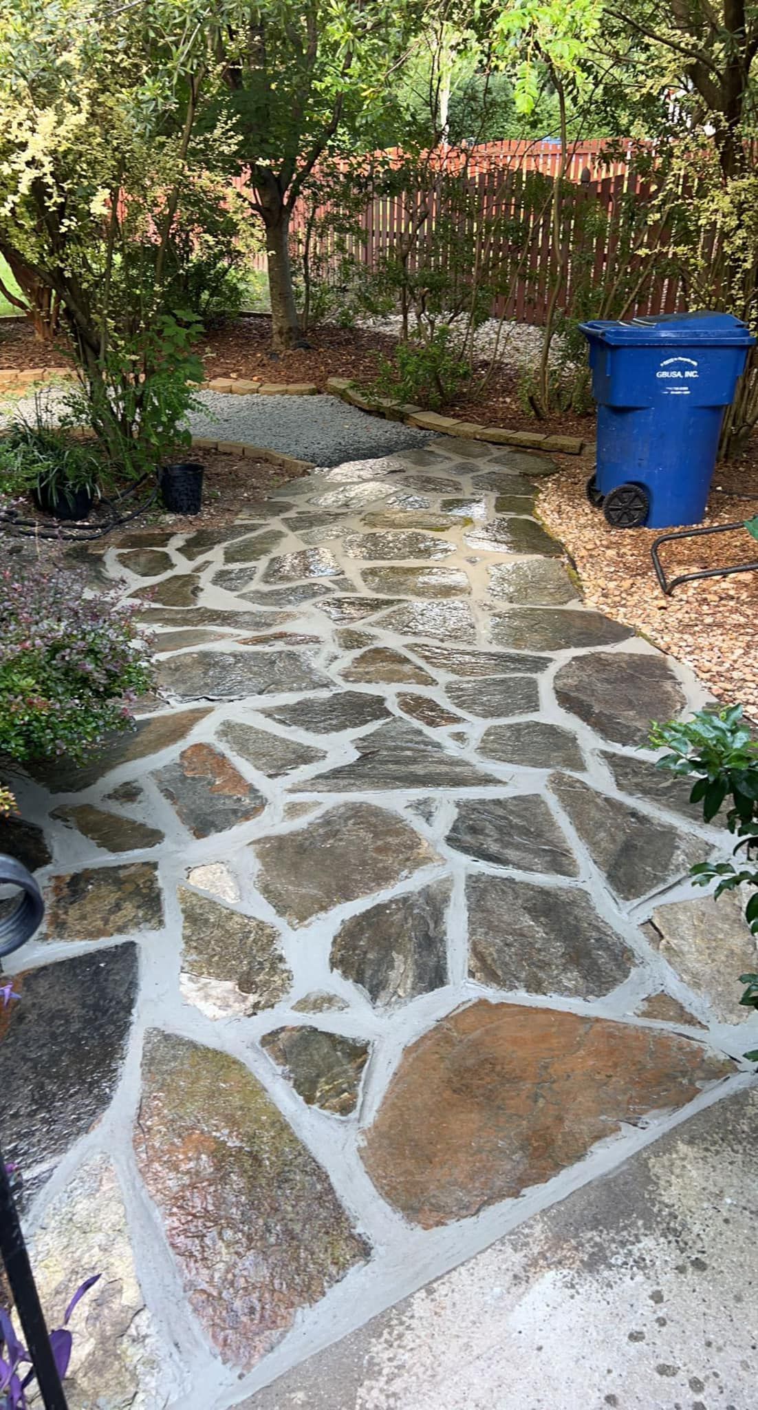A stone walkway with a blue trash can on the side of it.